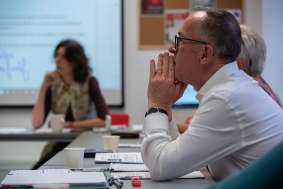 People engaged in a meeting, focused on a presentation displayed on a screen.